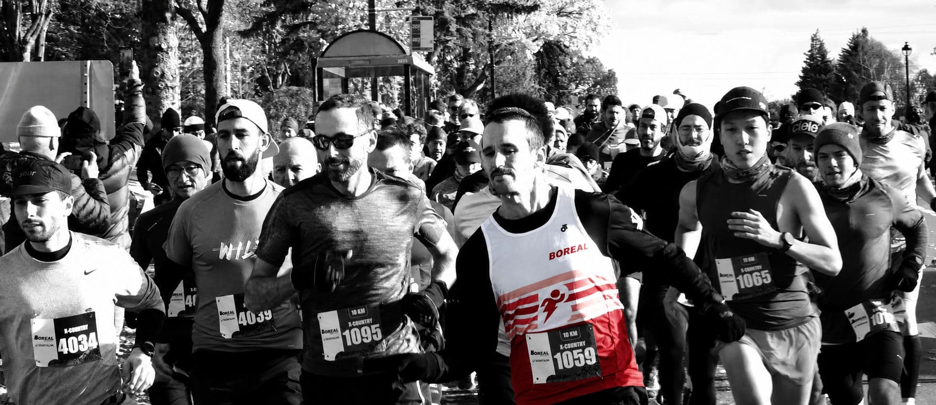 A pack of runners wearing race bibs at the start of a race, in black and white.