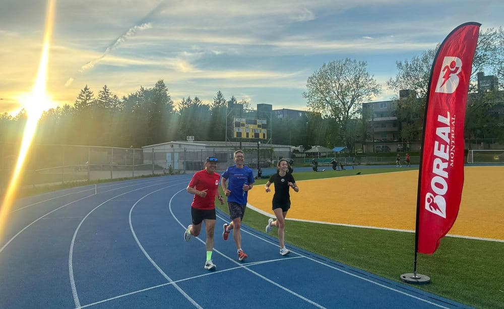 Trois coureurs sur la piste extérieure, à côté d’une bannière Boréal.
